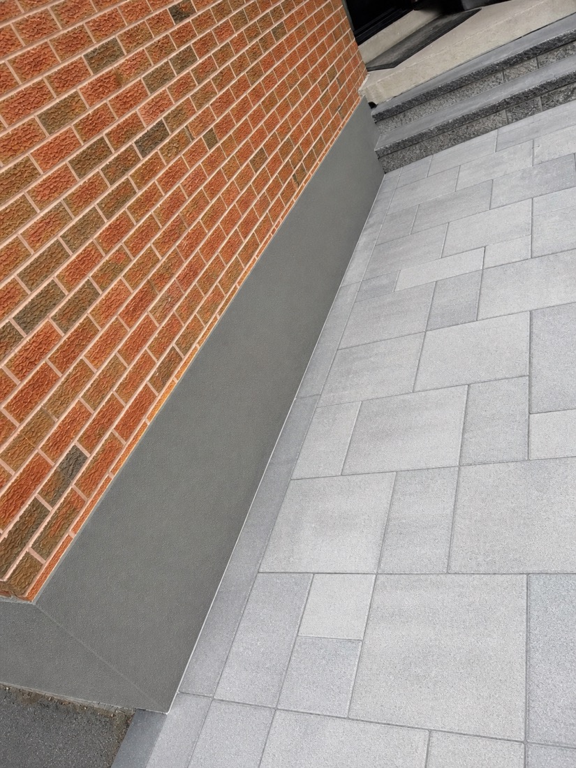 Close-up where fresh foundation parging meets a paver patio and brick wall at a GTA home