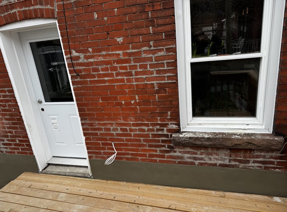 Fresh parge coat along the base of a red brick wall next to a wood deck on a Toronto home