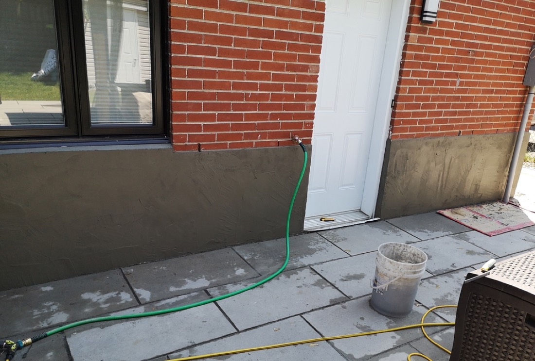 Newly applied parging curing along the base of a Hamilton brick home